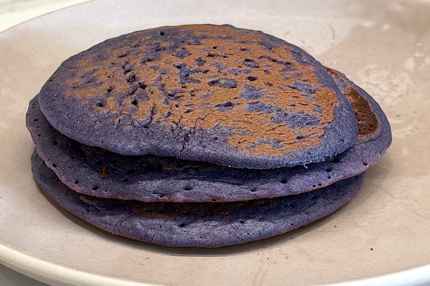 A stack of three purple ube pancakes on a plate